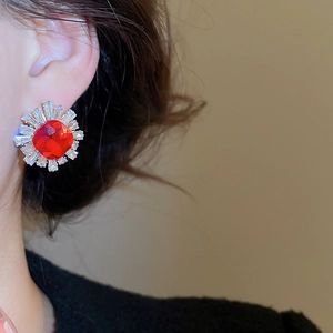 Close-up of vintage sunburst earring with red gemstone and clear zircon on ear