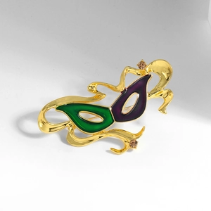 Elegant gold mask brooch with green and purple enamel finish and sparkling crystal accents