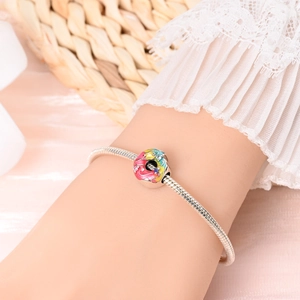 Detail of silver snake chain bracelet with colorful rainbow donut charm on wrist