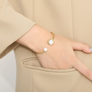 Detail of adjustable gold pearl bangle with white gemstone worn with beige suit