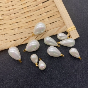 Teardrop imitation pearl pendants in various sizes with golden metal rings on bamboo mat