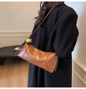 Detail of dark brown leather crescent bag with a yellow charm and rich texture