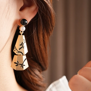 Detail of gold floral engraved trapezoid earrings with pearl and black bead tassels