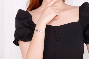 Close-up of a silver stainless steel pull bracelet with heart and flower charms on a model