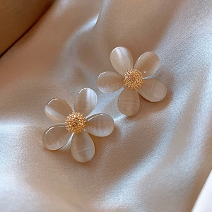 Detail of flower-shaped opal earrings in champagne gold finish on elegant silk fabric