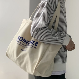 Detail shot of oversized beige canvas tote bag with blue text worn on shoulder