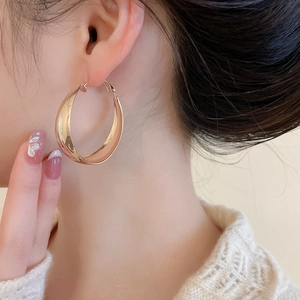Close-up of elegant gold round hoop earrings with wide curved design on a model