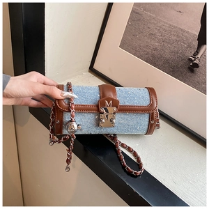 Close-up of denim cylinder bag with brown leather trim and metallic M-logo detail