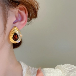 Close-up of a gold teardrop earring with a dark red gemstone and sparkling pavé diamonds