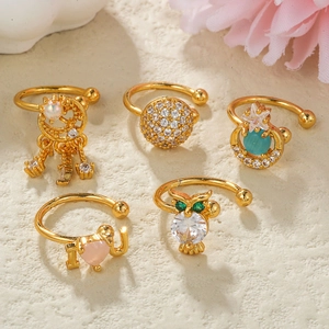 Set di cinque earcuff dorati con stelle, lune e ciondoli a cuore su superficie in pietra