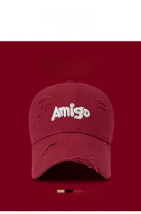 Detail view of burgundy baseball cap with white Amigo embroidery and distressed holes