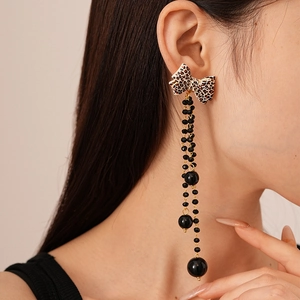 Close-up of leopard print bow earrings with long black beaded tassels on model