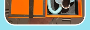 Close-up of a light blue braided leather keychain inside a vibrant orange gift box