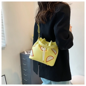 Detail view of yellow fruit-themed drawstring bucket bag on model with black blazer