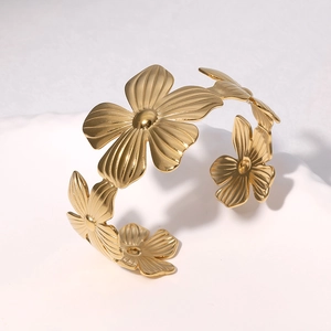 Golden five-petal flower open bangle with detailed radial texture on a white plate