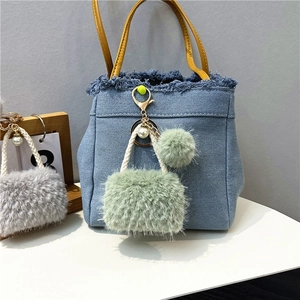 Detail of blue denim mini bag keychain with green faux fur pompom and pearl accents