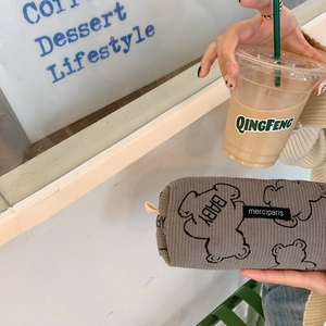 Detailed view of gray corduroy pencil case with baby bear print held in a cozy cafe setting
