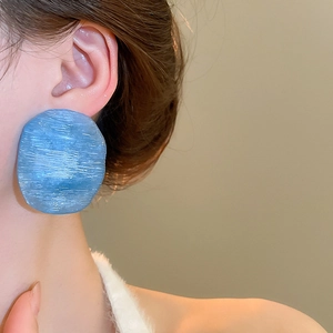 Detail of blue textured earrings with a brushed finish on a model showing a retro style