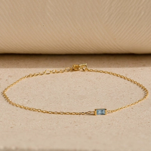 Elegant gold chain bracelet with rectangular blue birthstone on beige stone surface