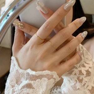 Close-up of minimalist thin gold-plated wave rings worn with elegant lace cuff