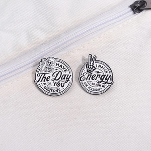 Detail of black and white skull enamel pins with creative text on a white canvas bag