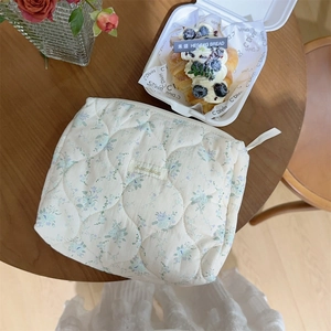 Detail view of the floral quilted makeup bag featuring a blue flower pattern and logo