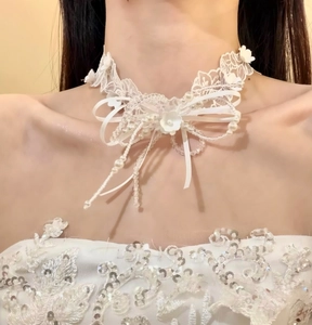 Dettaglio elegante di una collana girocollo in pizzo bianco con fiocco di perle e fiori