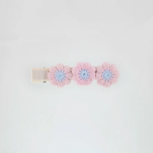 Detail of three embroidered pink and blue yarn flowers on a fabric-covered hair clip