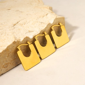 Nahaufnahme geometrischer quadratischer Goldohrringe auf einer Natursteinoberfläche