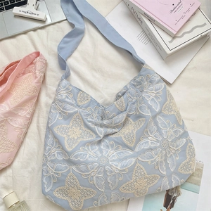 Close-up of elegant butterfly embroidery on light blue canvas shoulder bag texture