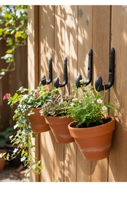 Vintage black cast iron J-hooks mounted on a wooden fence holding potted garden plants