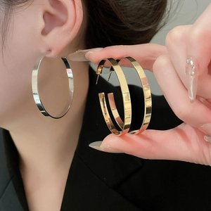 Detail of wide flat metal hoop earrings shown in polished gold and silver finishes