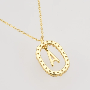 Close-up of golden oval hollow pendant with letter A on a delicate cross chain