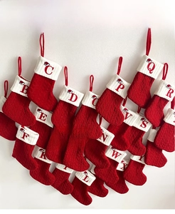 Macro detail of red cable-knit Christmas stockings with white cuffs and letter embroidery