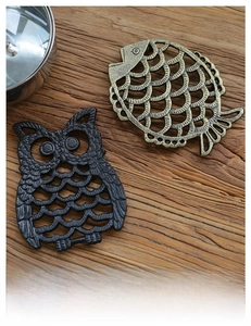 Close-up of retro owl and fish cast iron trivets on a rustic wooden table surface