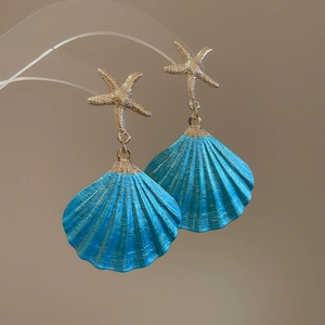 Detail of gold starfish earrings with blue shell pendants for beach vacation style