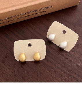 Detail view of gold and silver teardrop stud earrings on beige card display