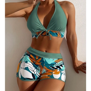 Detail of dark green halter bikini top and high-waisted botanical leaf print swim shorts