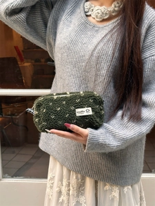 Macro shot of fluffy dark green plush pencil case with white floral pattern and zipper