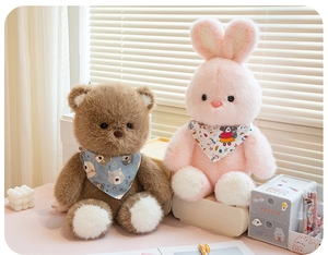 Detail of plush brown bear and pink rabbit dolls with cartoon scarves on a desk