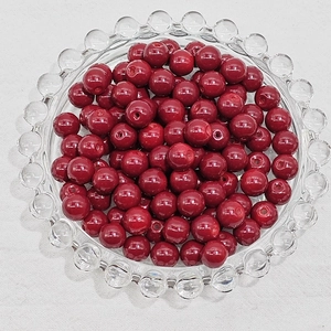 Detailed view of dark red polished glass beads on a transparent tray for DIY jewelry