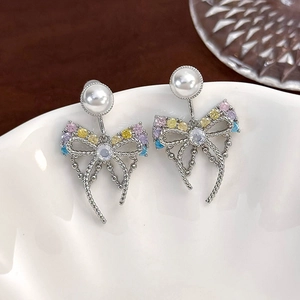 Macro shot of silver bow earrings with colorful zircons and pearls on white ceramic