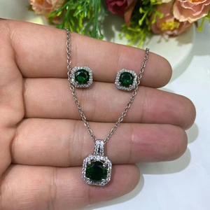 Macro shot of silver jewelry set with green emerald-cut stones and zircon accents