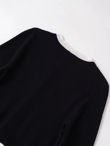 Close-up of black ribbed knit cardigan featuring contrast white collar and shoulder stitching