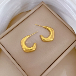 Macro view of gold minimalist C-shape hoop earrings on a beige velvet jewelry box