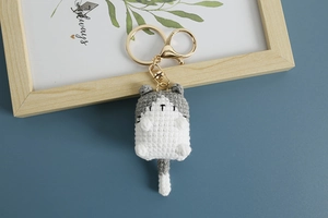 Close-up of handmade crochet cat keychain with grey and white yarn and golden metal ring
