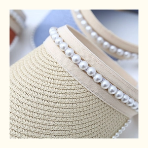 Detailed close-up of khaki straw sun hat featuring pearl trim and woven texture
