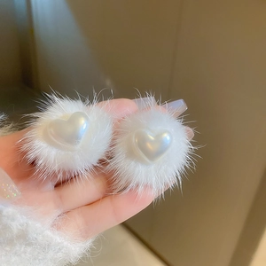 Close-up of fluffy white faux fur earrings featuring a glossy heart-shaped pearl center