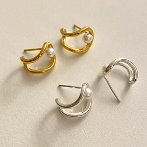 Detail of C-shaped polished silver and gold earrings with small pearls on beige base