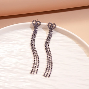 Close-up of heart-shaped purple rhinestone earrings with long tassels on a ceramic tray